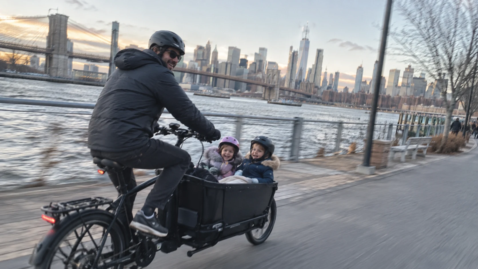 Ben riding a cargo bike with Lily and Leo along the Brooklyn waterfront